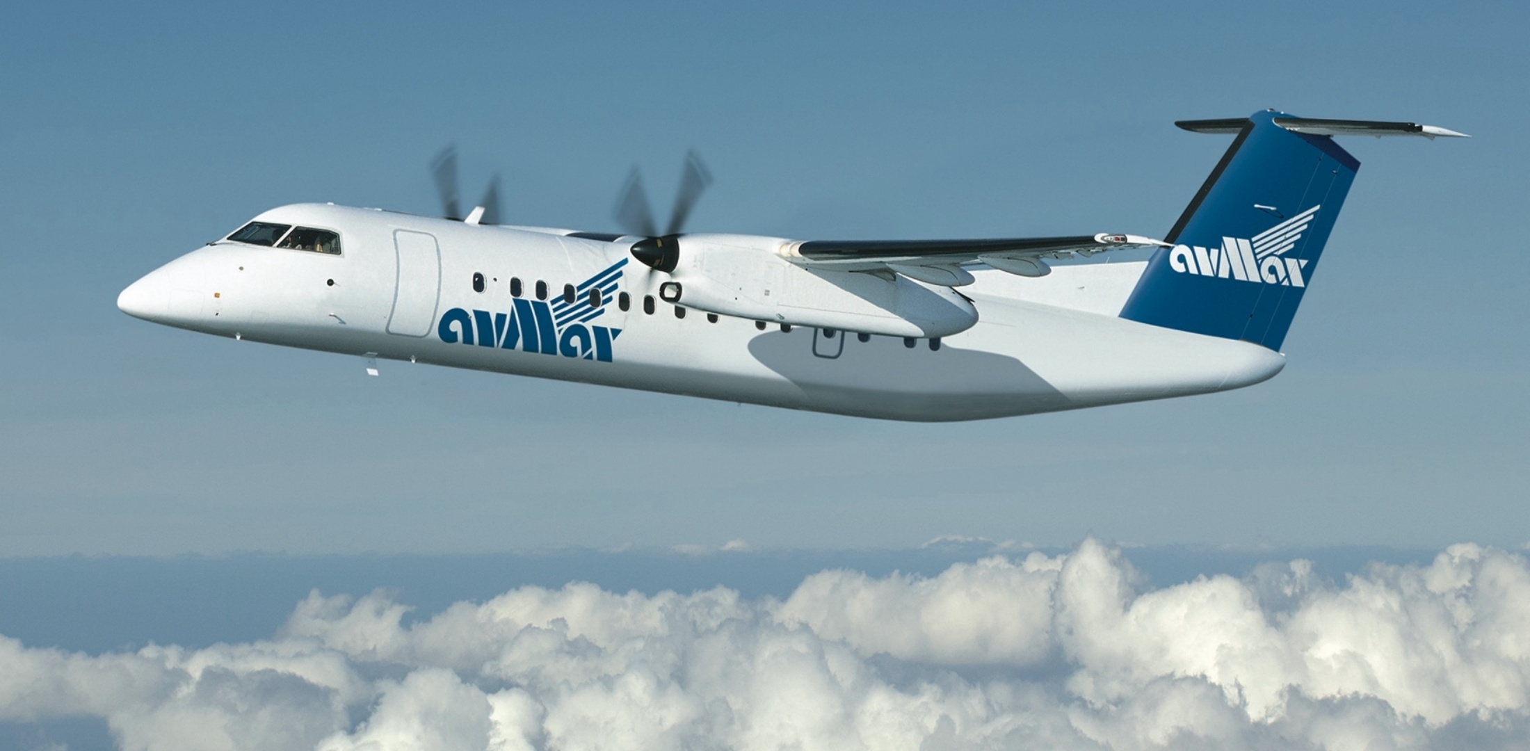 An Avmax Dash 8-300 flies above a layer of clouds.